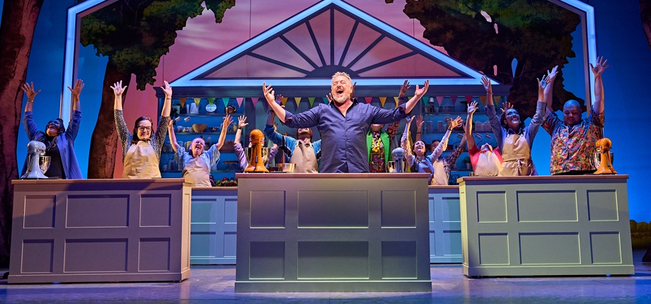 Cast members of the Great British Bake Off Musical from the West End, hands in the air.