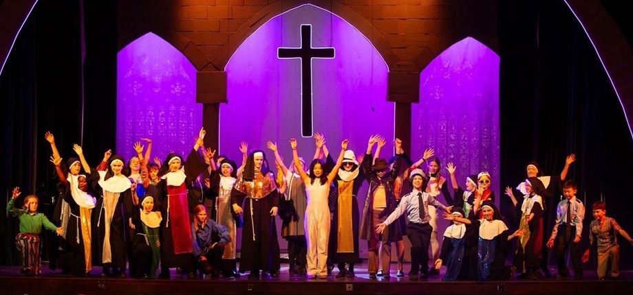 School production of Sister Act musical. Cast with hands in the air in front of a cross and church arches